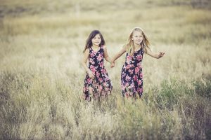 Two girls in dresses running in a field.