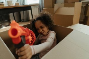 A girl in a moving box with a toy gun