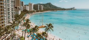 Apartment and condo buildings with sandy beach, palms and many people taking sunbath or walking in the ocean, you will find after Moving from Pompano Beach to Miami Beach.