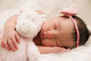 A small baby girl sleeps hugging her favorite toy.