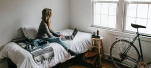 A girl sitting on the bed and working on the computer as one of international students moving to Miami
