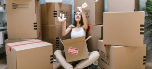 A girl sitting on the floor among the moving boxes throwing paper confetti in the air