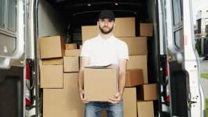 A mover holding a moving box in front of his van full of movign boxes