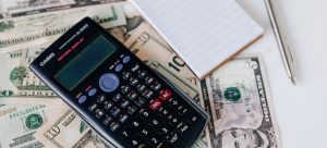 A caluclator and a notepad places on top of the money and a pen next to all of that;