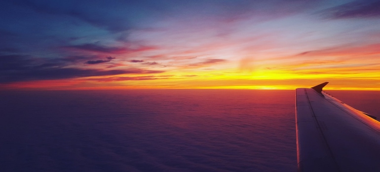an airplane wing with the ocean and the sunset in the background of it, depicting one of the best ways for moving from LA to Miami in less than ten days
