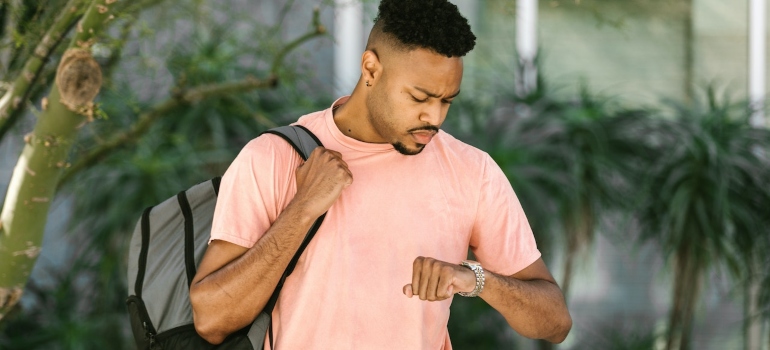 a man in a pink shirt and a backpack on looking at his watch