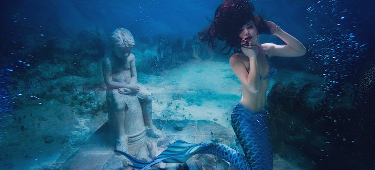 Underwater photo of a mermaid in front a statue