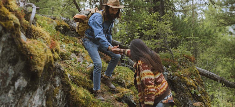 A man and a woman climbing on a rock during their hike.
